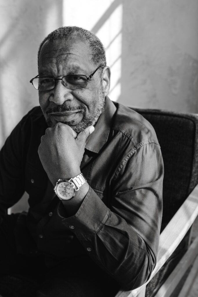 Monochrome portrait of an elderly man with glasses, sitting thoughtfully indoors.